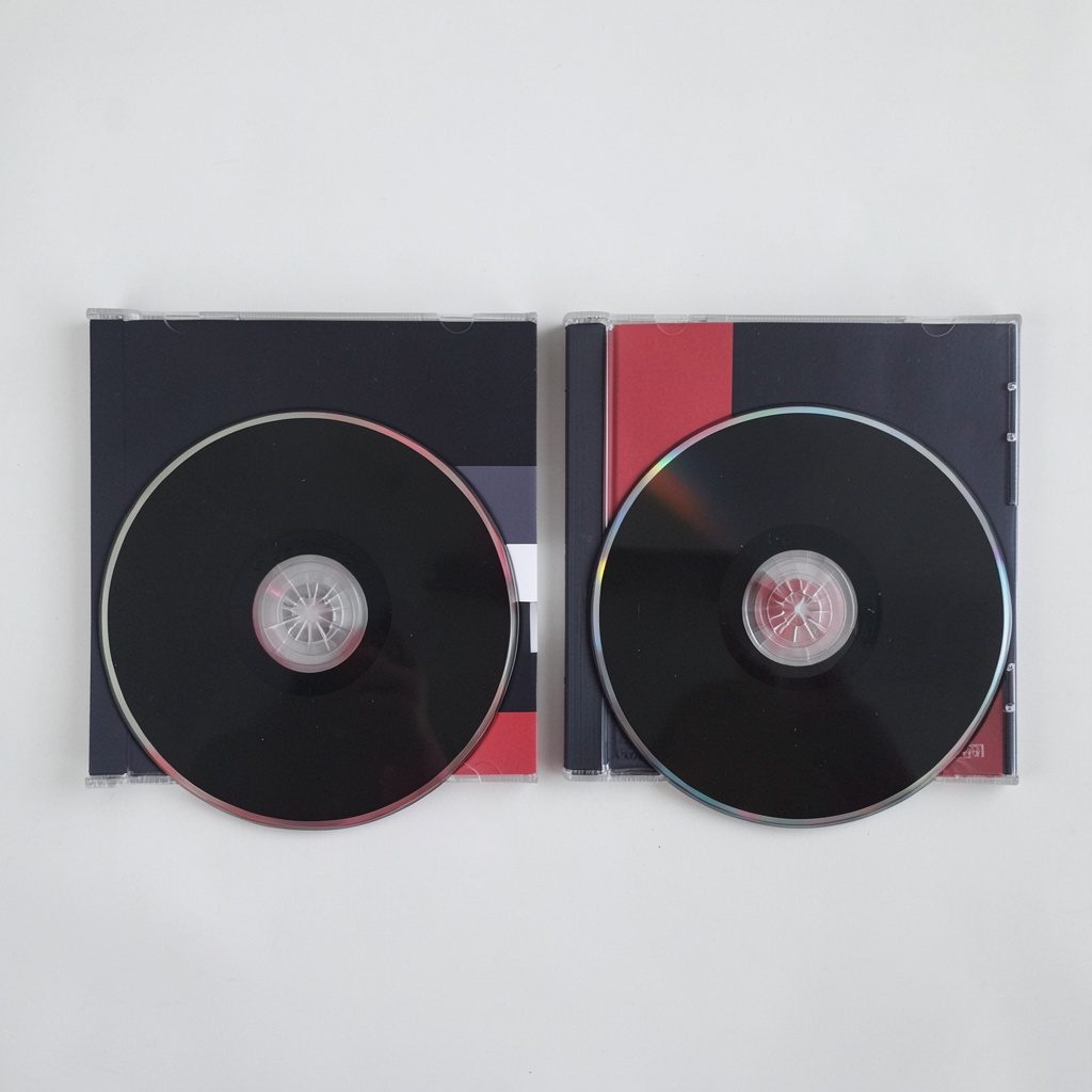 Dos discos compactos sobre una portada de álbum doble, colores oscuros con detalles en rojo y blanco.